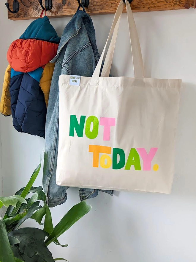 A hanging natural canvas tote bag with multi coloured Not Today slogan.