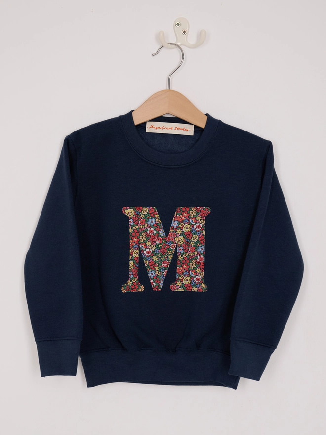 a kids navy sweatshirt with the initial M personalised in floral liberty print on the front