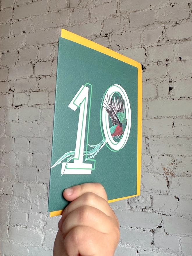 Deep green card featuring a big white number 10 and an illustration of a quetzal bird alongside a yellow envelope