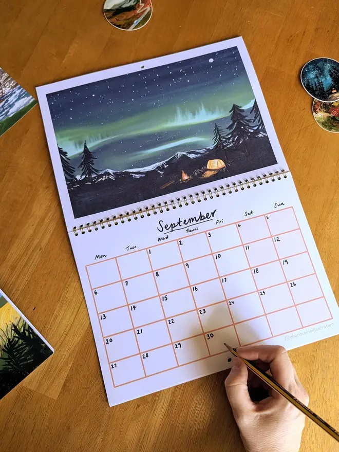 Illustrated wall calendar featuring an artwork of the northern lights with a camping tent underneath