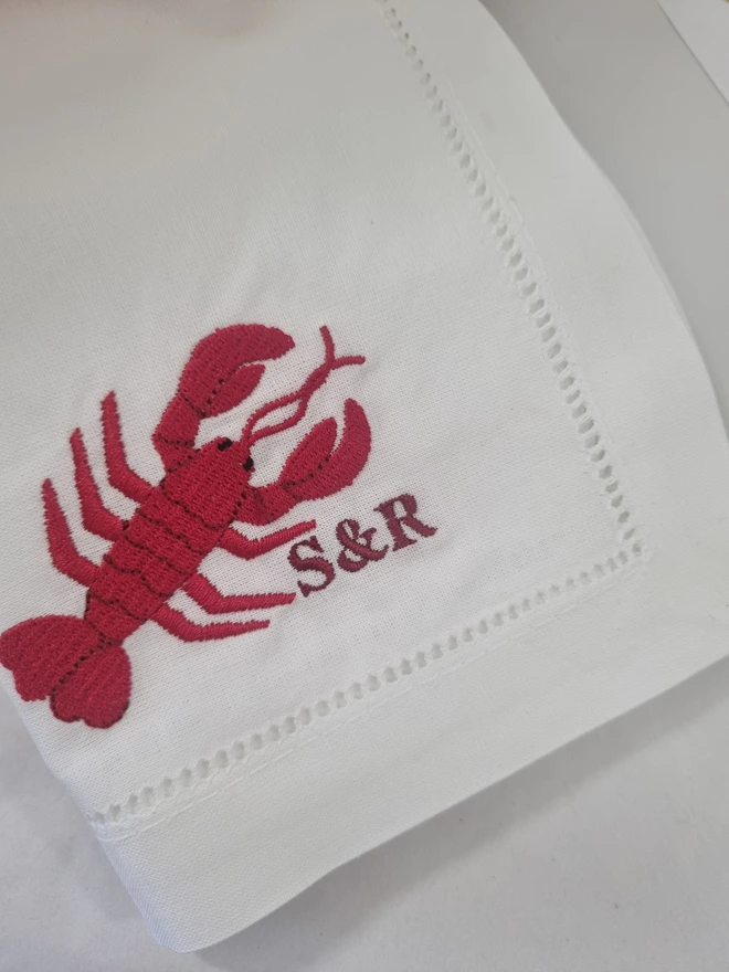 A white napkin with a red lobster embroidered on it with the initials S&R