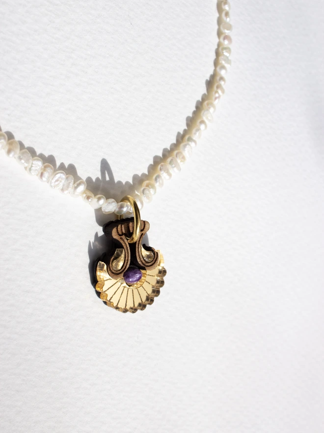 Pearl necklace with a shell shaped gold pendant & gemstone on a white background