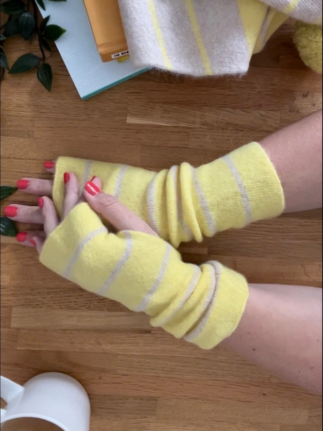Yellow knitted wristwarmers shown worn with hands stretched out on table