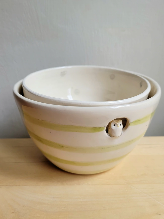 2 bowls on a wooden counter top with the small bowl inside the green and cream stripy bowl with an owl perched in the circular hole 