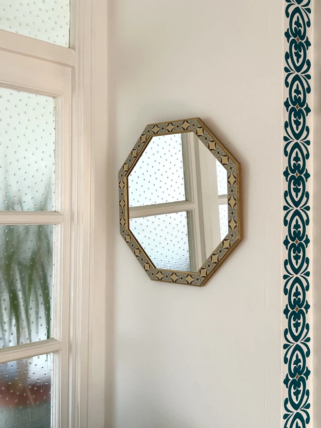 Medium sized octagonal wall mirror with a hand painted decorated frame with gold stars and blue star burst repeating pattern around the frame