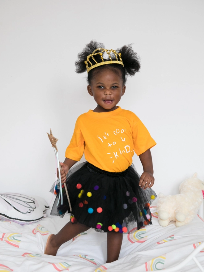 Little girl wearing a pom pom tutu wearing a crown and holding a wand.