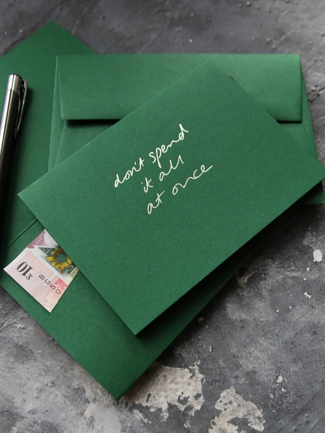 Hand foiled cash card or money wallet in a forest green colour handfoiled in shiny lime green text which says 'don;t spend it all at once'.