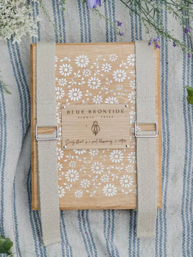 Wooden Flower Press with Straps - Delicate Daisy birds eye shot of the flower press on a blue striped blanket