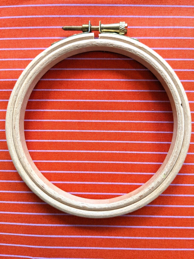 A wooden embroidery hoop lying on a stripy red fabric