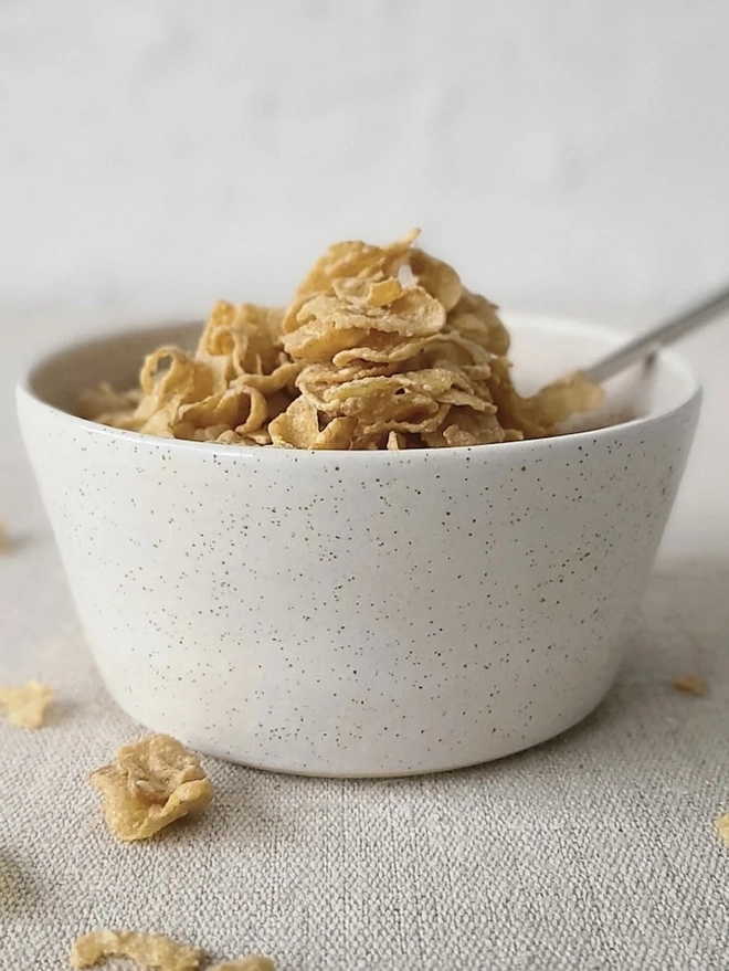 Classic Ceramic Breakfast Bowl, a breakfast bowl sitting on a grey carpet against a plain backdrop. It is accompanied by some cereal and a spoon. 
