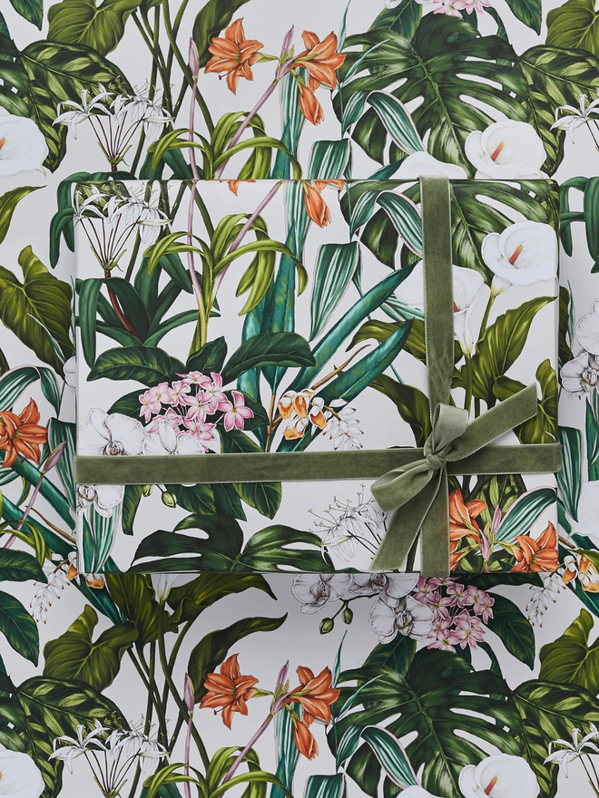 palm house tropics floral gift wrap sheet. a box wrapped in white illustrated leafy gift wrap with a purple ribbon.
