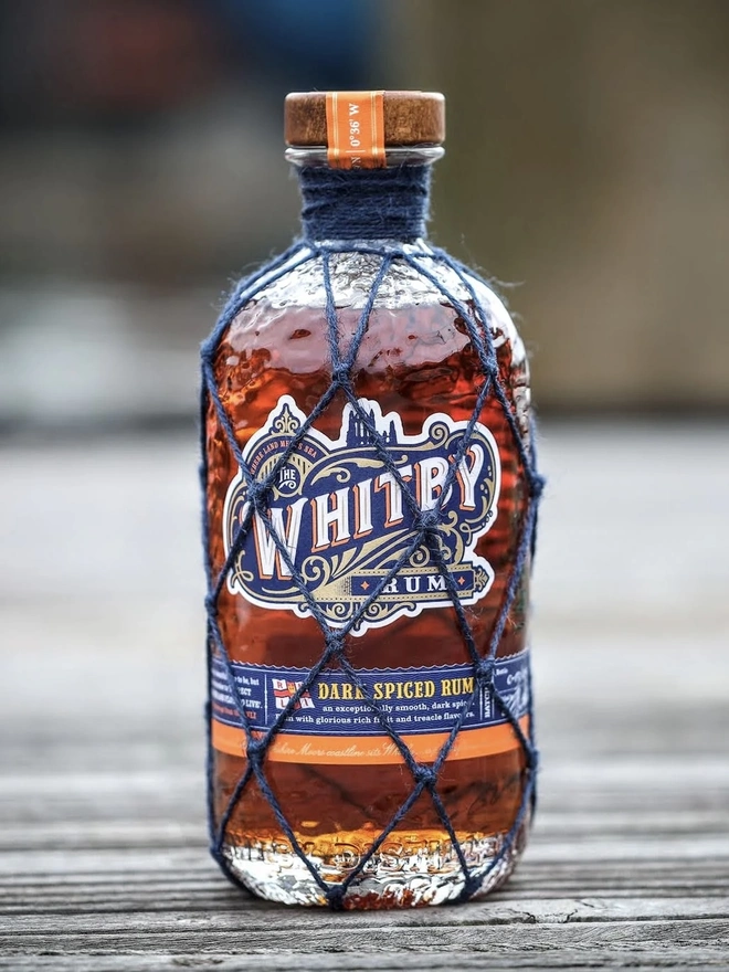 Whitby Dark Spiced Rum - RNLI Edition, a bottle of rum sitting on a wooden surface outside. 