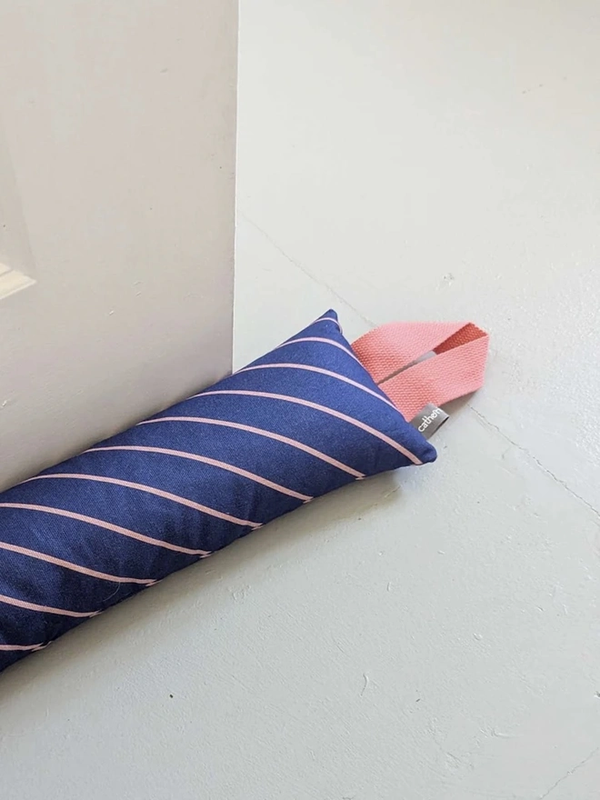 Draught Excluder, a colourful patterned draught excluder sitting on the floor by a white door. 