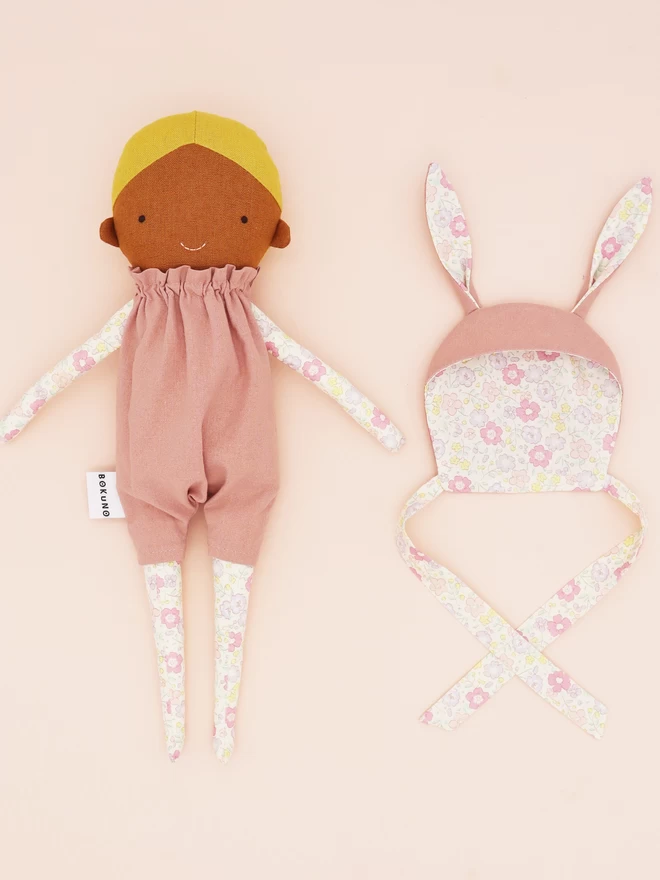 brown skin girl doll with pink floral outfit and bunny ear bonnet