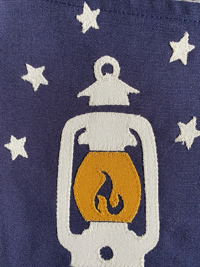 Detail of a navy canvas 'Seek Adventure' pennant flag showing the canvas hurricane lantern with canvas stars.
