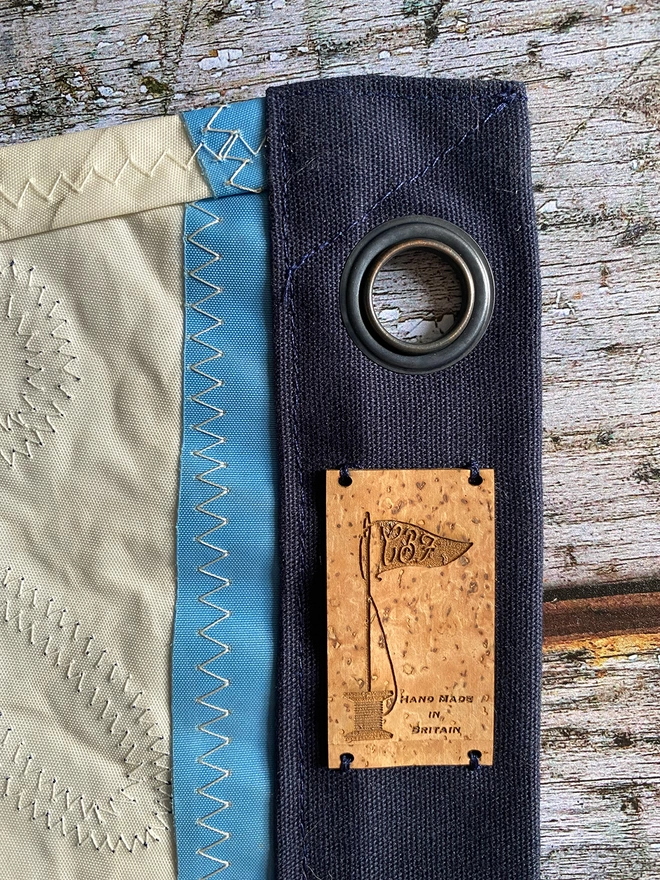 A photo showing the reverse side of an up cycled sail cloth 'Keep the sea plastic free' pennant showing the stitch work on the back with a hanging eyelet and cork label.