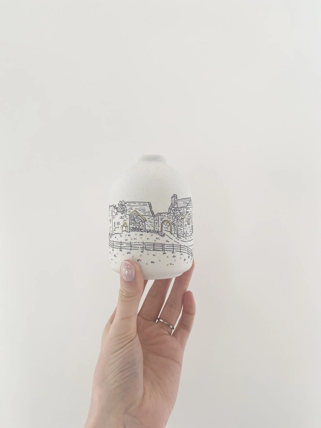 A ceramic vase with black line drawing of wedding venue being held on a woman's hand