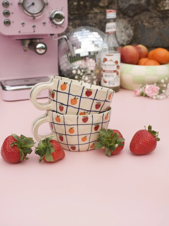 handmade stoneware pottery mug with a blue grid design and handpainted strawberries and oranges