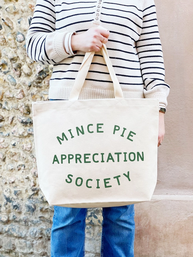 a model holding a large natural canvas tote bag bearing the words mince pie appreciation society