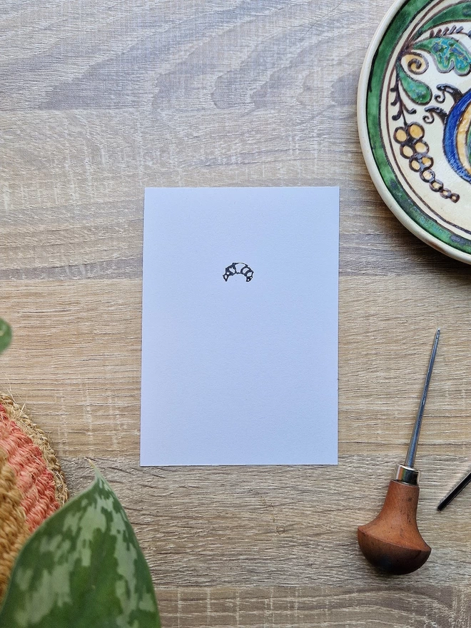 A tiny croissant lino print on a white A6 page