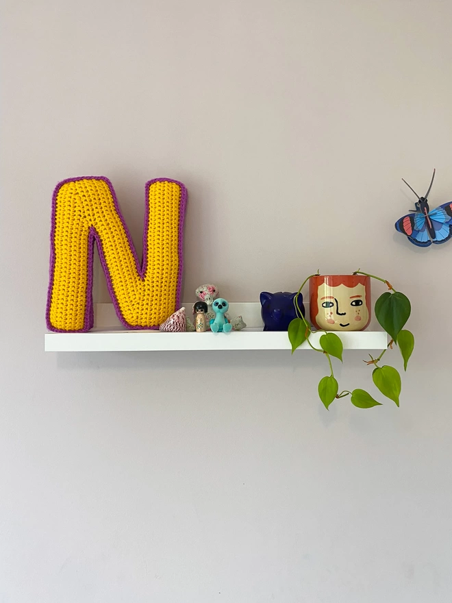 Crocheted N Cushion in Sunshine Yellow & Magenta, on child's shelf