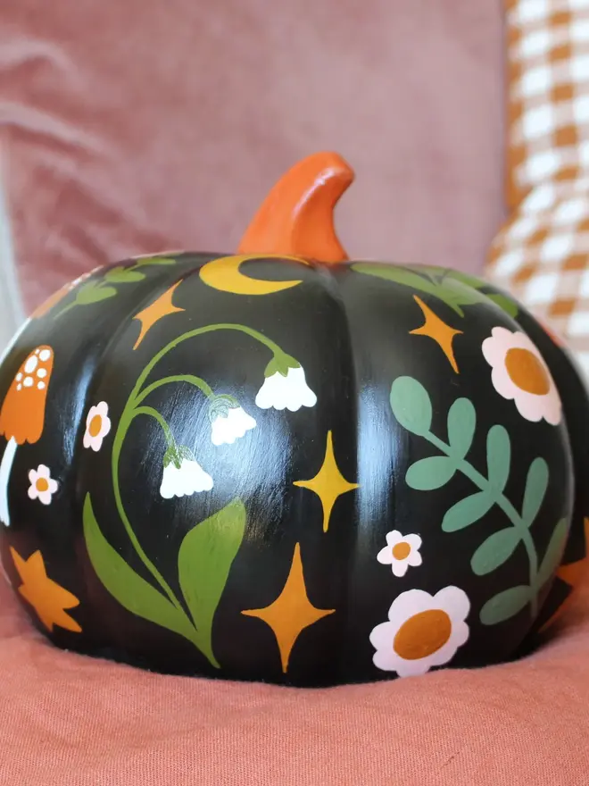hand-painted folk art ceramic pumpkin. a black ceramic pumpkin painted with mushrooms and flowers.