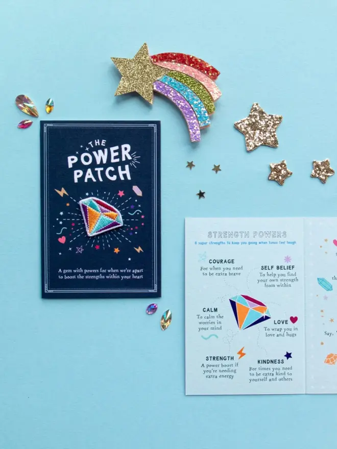 The navy patch card reads "A gem with powers for when we're apart to boost the strengths within your heart." Next to it, a pale blue fold-out card lists six "Strength Powers," including courage, calm and kindness.