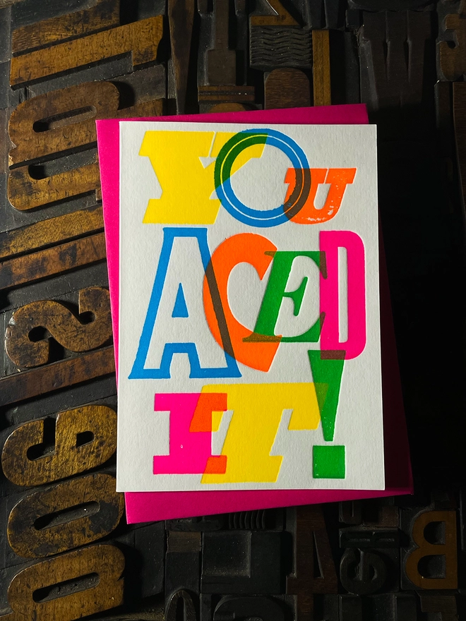 Colourful typographic letterpress card with bold overlapping neon letters spelling ‘You Aced It!’, perfect for celebrating exam success.