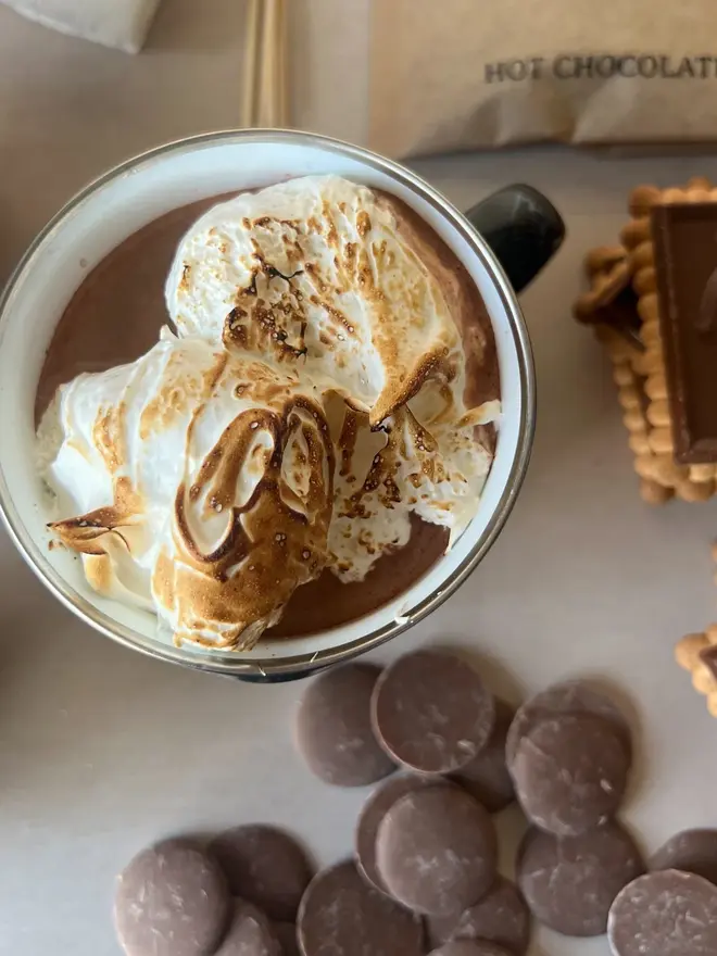 Luxury S'mores & Hot Chocolate Kit, a hot chocolate and chocolate above a marble surface. In the background, the rest of the kit lies. 