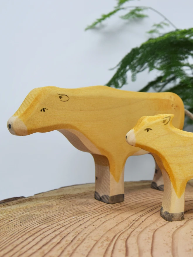 wooden toy cow and calf on wood slice with plant in background