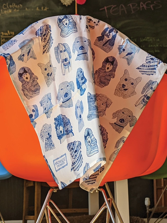 blue dogs 100% organic cotton charity tea towel hanging over the back of an orange chair 