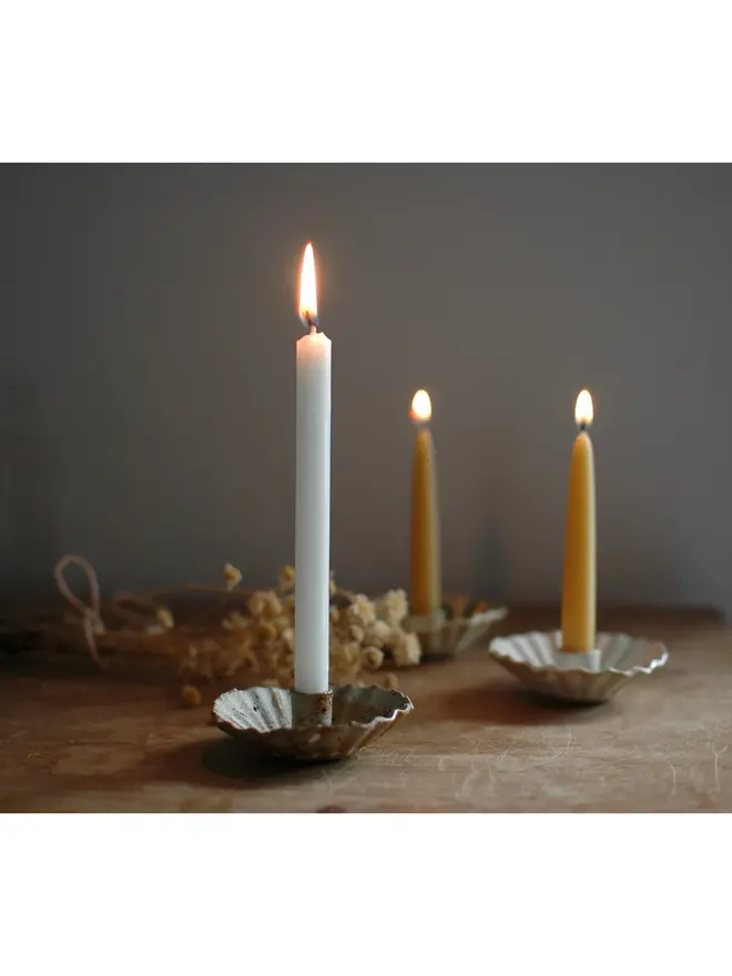 Handmade Natural Speckled Ceramic Candlestick Holder, a group of ceramic candlestick holders sitting on a wooden surface. They are accompanied by some candles. 