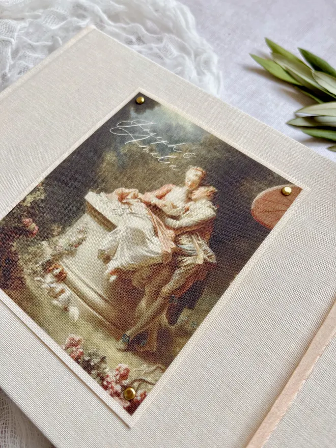 Luxury fabric printed wedding guest book featuring an images of lovers from an 18th century rococo work of art. Linen covered book finished with ribbon