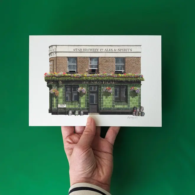 Greenwich The Pelton Arms Pub Giclée Print (Unframed), a print of a brown and green pub sitting against a green backdrop. It is being held by someone. 