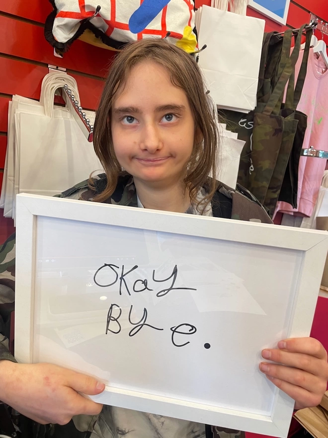 Piper a autist, deaf, teenager from Hackney  holds her artwork in a white frame. Her unique black handwritten font on a white background