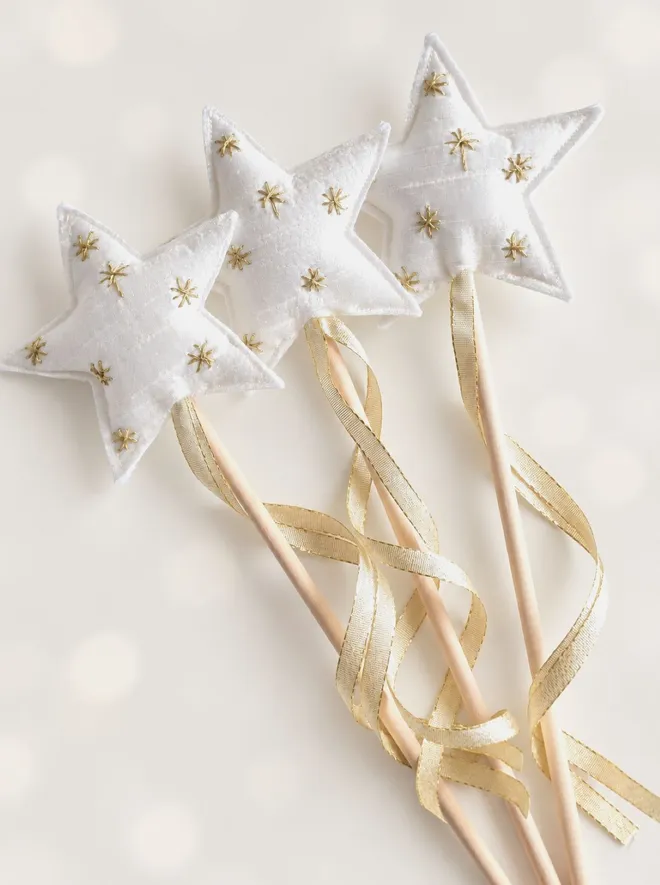 Close-up of three handmade white silk star wands with gold embroidered stars and trailing pale gold ribbon.