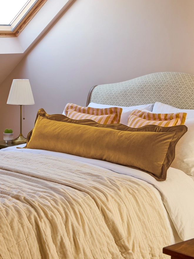 Handmade scalloped mustard velvet bolster cushion 130cm with feather pad paired with stripe linen cushions on bed, Kika Bespoke