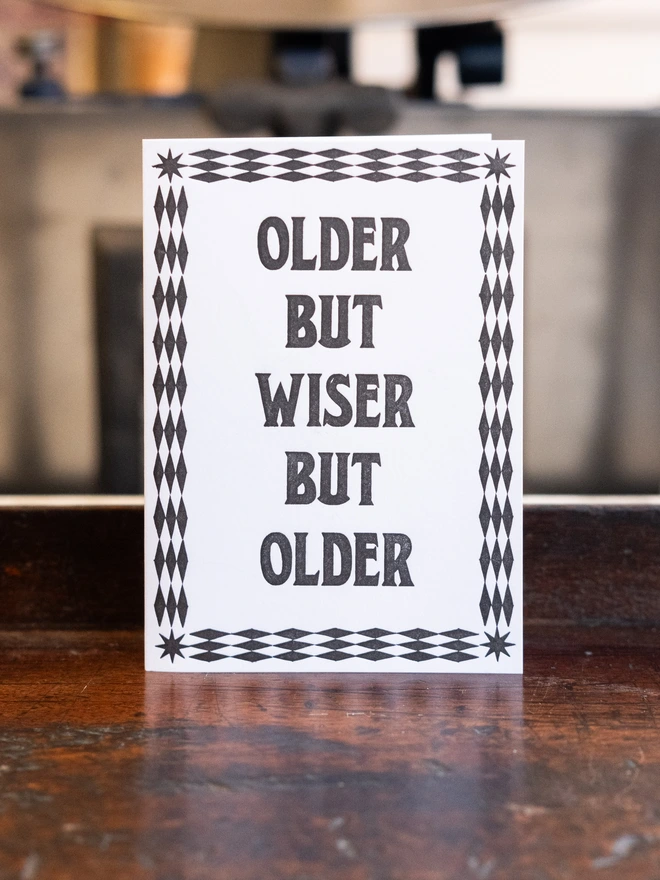 Letterpress card with text design, "Older but wiser but older," bordered by art-deco pattern of diamonds and stars.