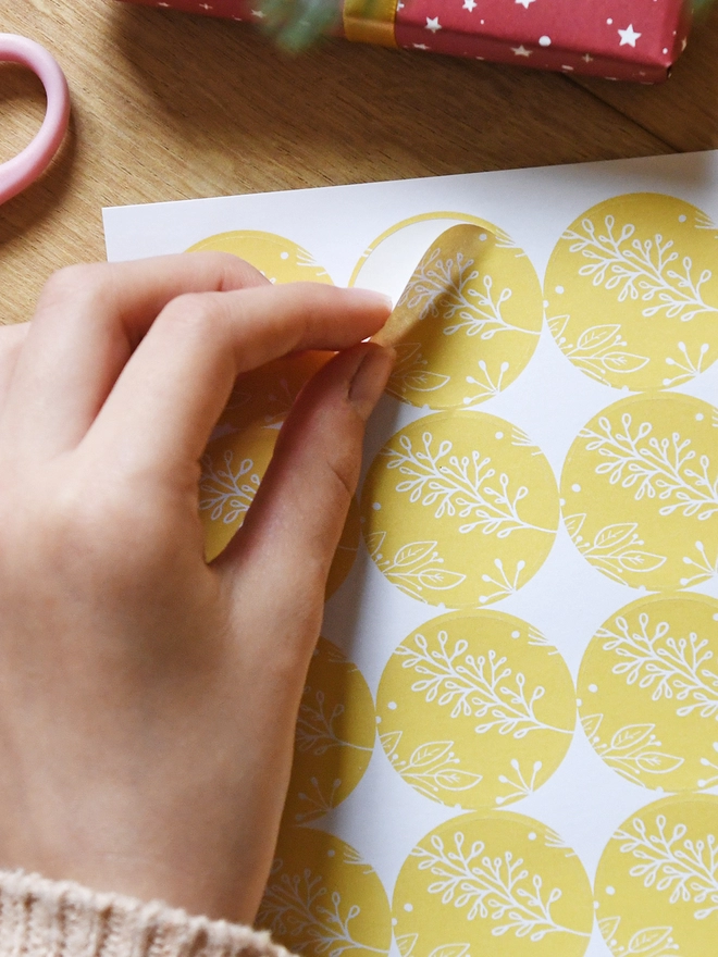 A round yellow sticker with a gentle botanical design is being peeled from a sheet of 35 matching stickers.