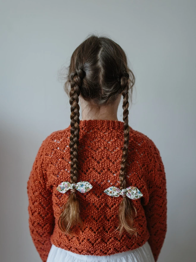 Back view of little girl in rust autumnal jumper and long plaits with liberty hair bobbles