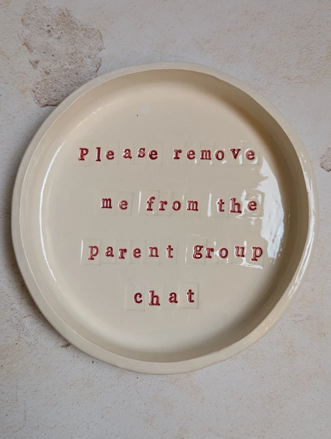 Please remove me from the parent group chat a ceramic dish sitting on a grey surface. It is inscribed with a message in red writing. 