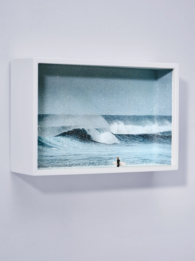Miniature scene in an artbox showing a tiny male surfer watching the ocean
