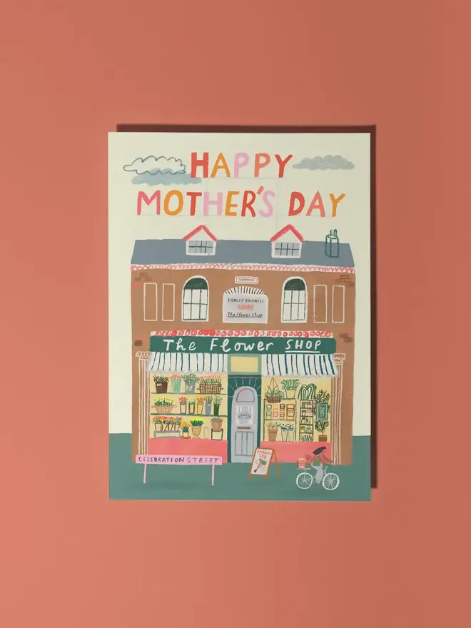 flower card illustrated mothers day card. brick flower shop building illustrated on beige background with 'happy mothers day'.