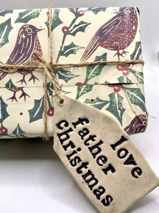 'Love Father Christmas' Handmade Ceramic Gift Tags, a ceramic gift tag attached to a gift sitting on a plain white surface. 
