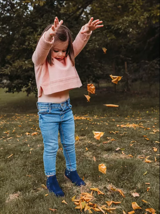 Little girl throwing leaves wearing Navy suede chelsea boots with a blue dinosaur print