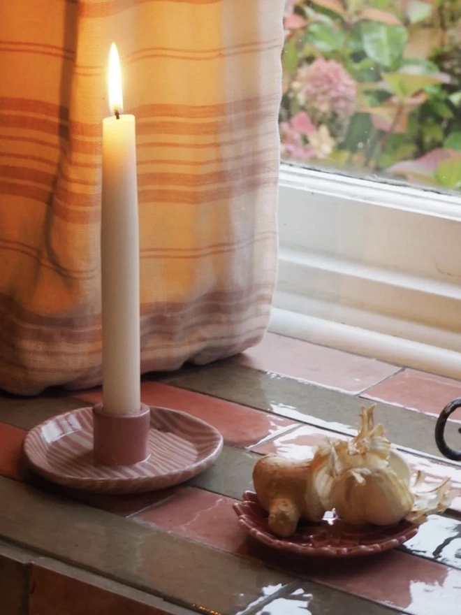 Ceramic Patterned Candlestick Holder, a pair of colourful candlestick holders sitting on a window sill. They are accompanied by a lit candle. 