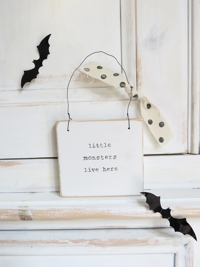 hand painted white wooden sign with hand painted little monsters message