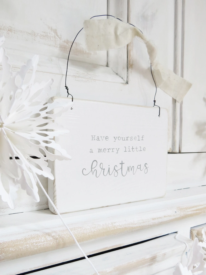 white wooden sign painted with a merry little Christmas message hung on wire and decorated with ribbon