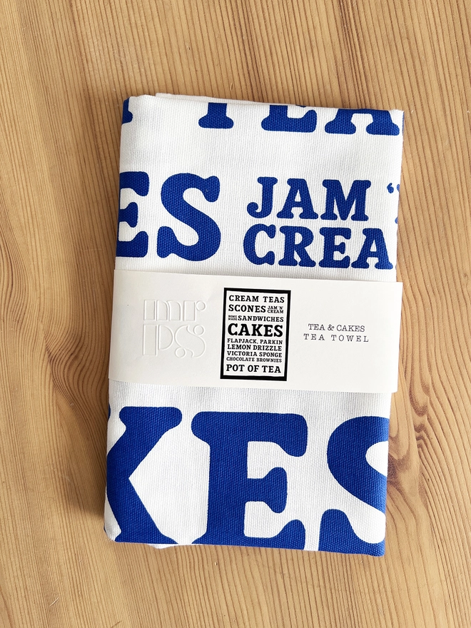 Mr.PS Cakes menu tea towel folded on a pine table