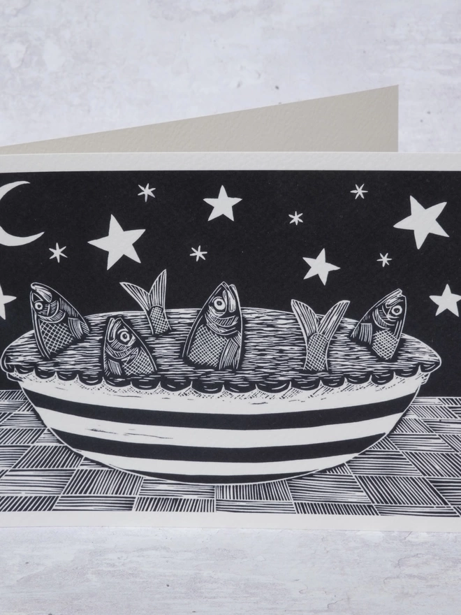Greeting Card with an image of a Fish Pie in a stripey dish, with the fish gazing up at the stars in the sky, taken from an original lino print